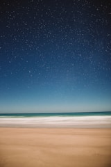 A serene landscape with soft waves lapping at a tranquil shore under a starry sky.