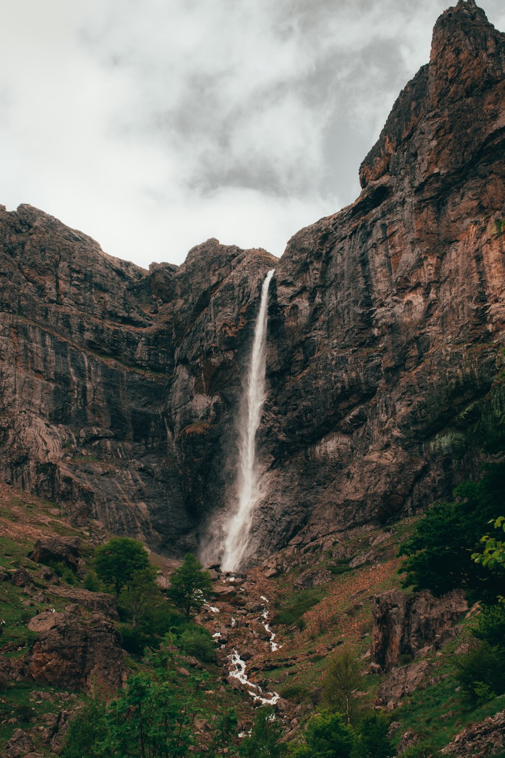 waterfalls on rocky mountain under cloudy sky during daytime