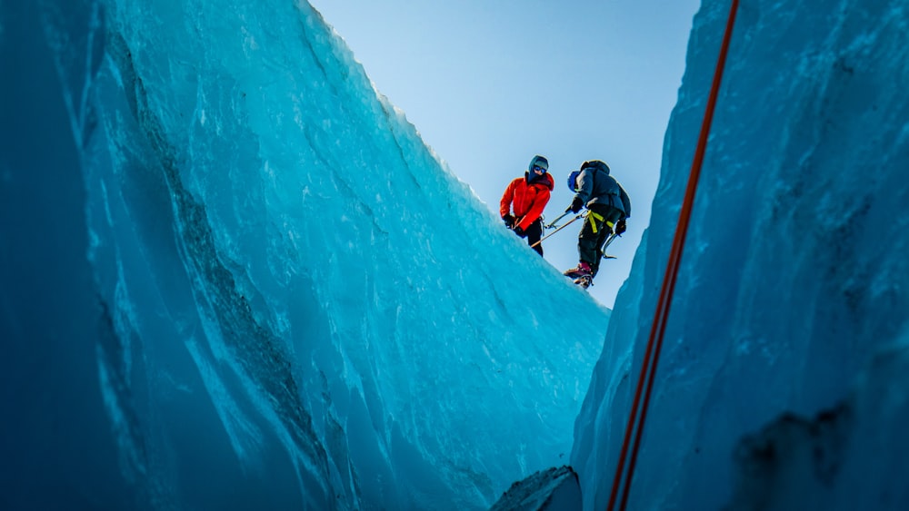 2 person in red jacket and black pants riding on snow ski