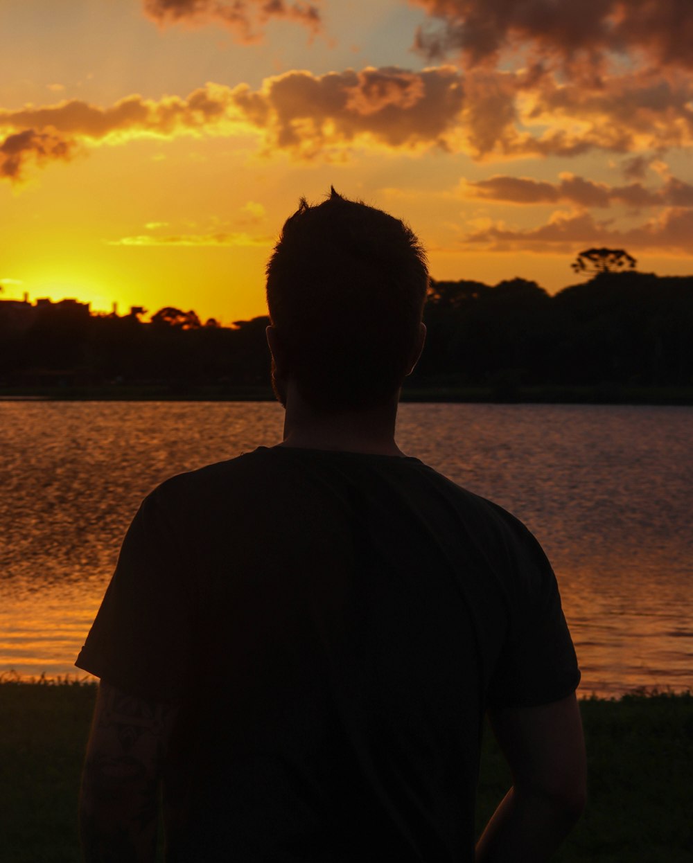man in black shirt standing near body of water during sunset