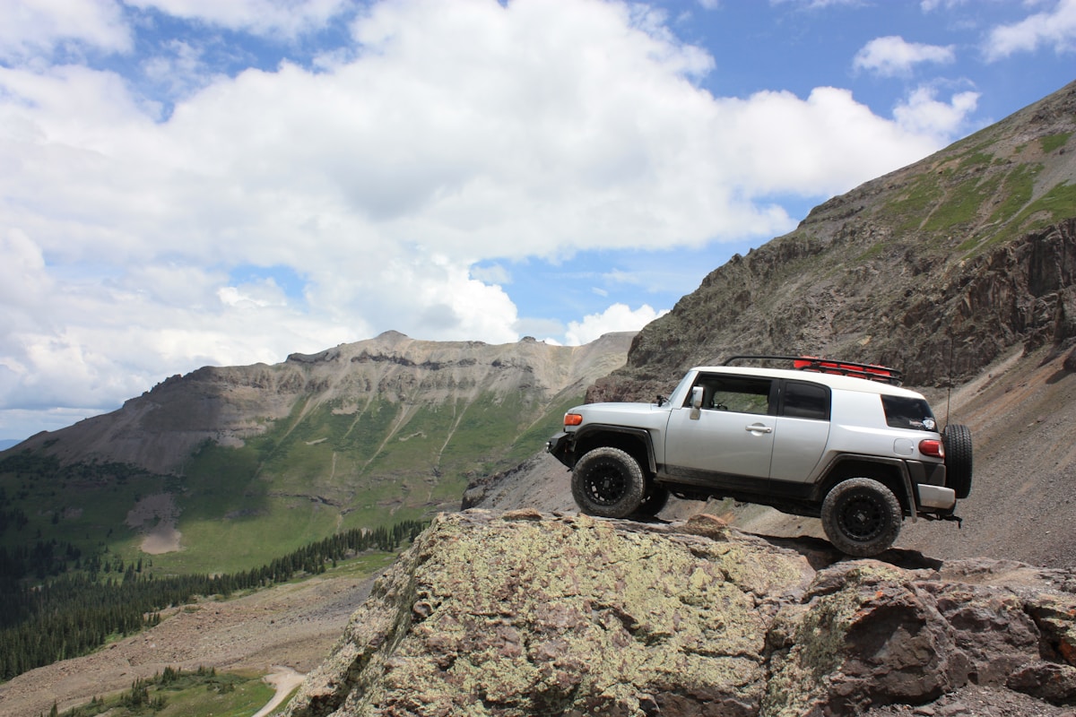 High-clearance truck navigating a rugged Colorado mountain pass dirt road during summer