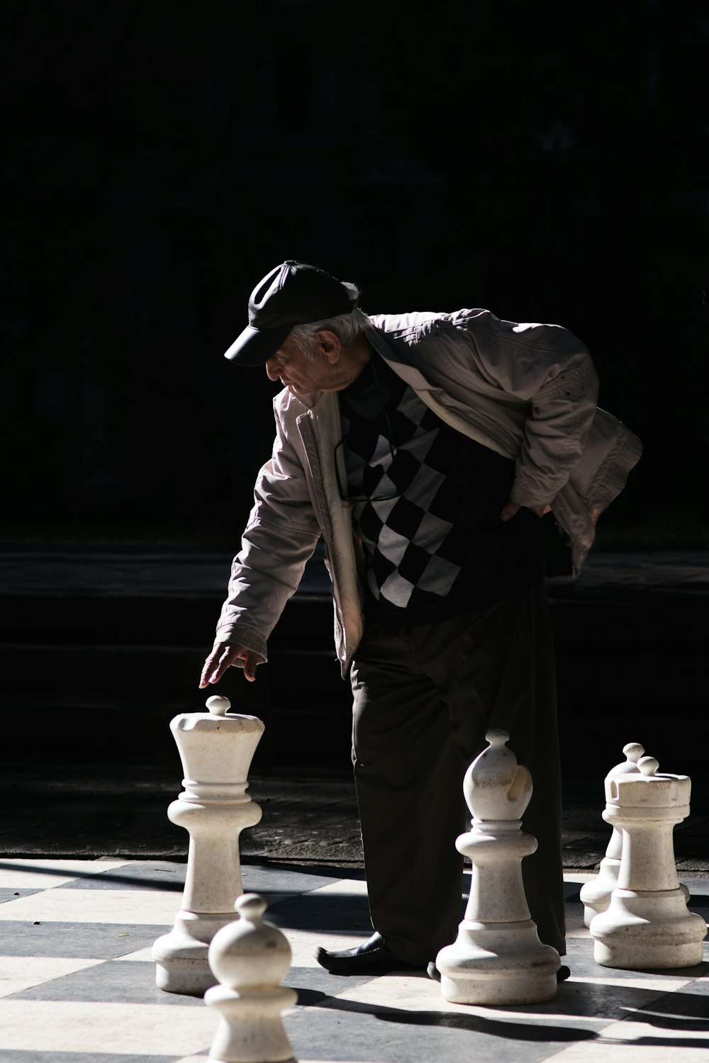 Hombre en chaqueta blanca y negra y pantalones negros de pie junto a una pieza de ajedrez blanca