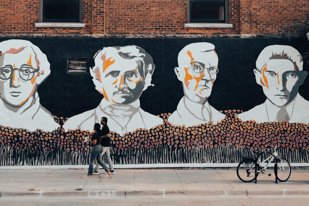 people walking on sidewalk near wall with graffiti during daytime