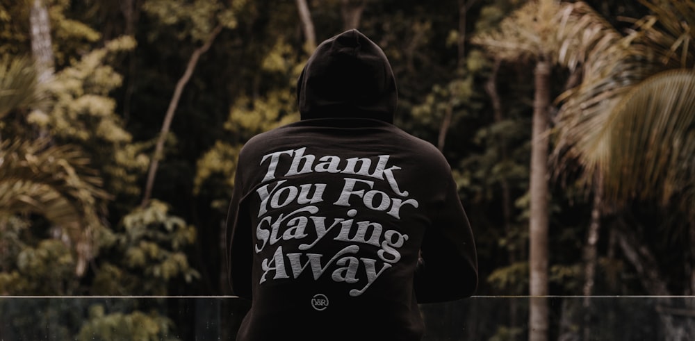 man in black and white hoodie standing near trees during daytime