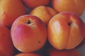 A cluster of ripe apricots with a soft, fuzzy skin in shades of orange and red. The fruits are closely packed together, showing their natural texture and small blemishes.
