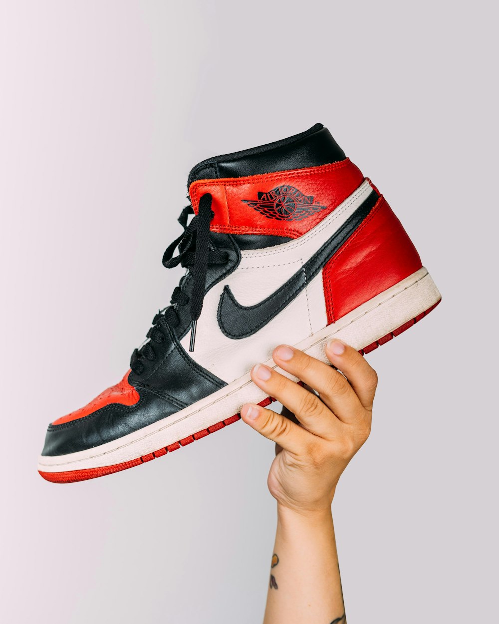 person holding red and white nike air jordan 1 shoe