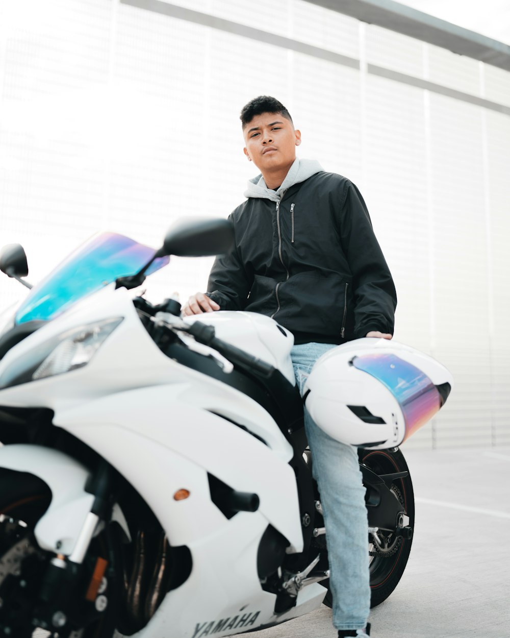 man in black jacket standing beside white and blue sports bike