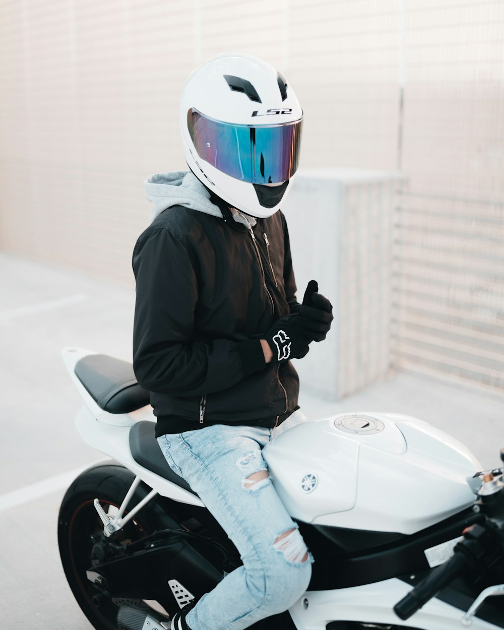 man in black jacket and blue denim jeans wearing white helmet sitting on white motorcycle during