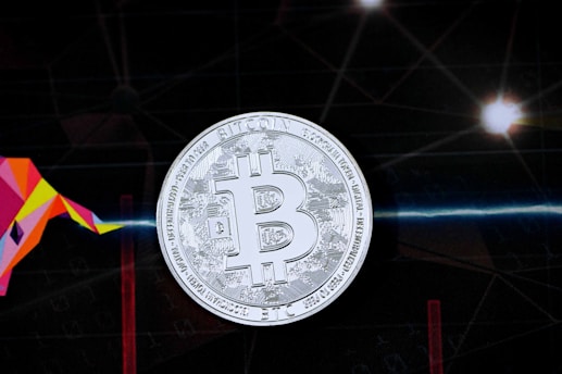 A silver Bitcoin symbol is prominently displayed against a dark background that features a geometric bull shape in vibrant colors on the left side. The background is interspersed with subtle digital patterns and flares of light that suggest a technological or futuristic theme.