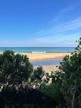 A serene beach view with gentle waves and a clear blue sky.