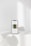 A smartphone displaying a minimalist webpage stands on a white surface, with soft shadows cast around it. The background is a pale, neutral tone with subtle lighting.