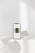 A smartphone displaying a minimalist webpage stands on a white surface, with soft shadows cast around it. The background is a pale, neutral tone with subtle lighting.