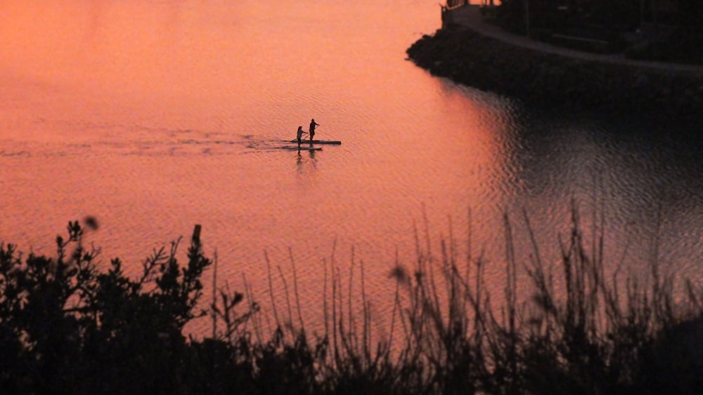 silhouette of person riding on boat on body of water during sunset