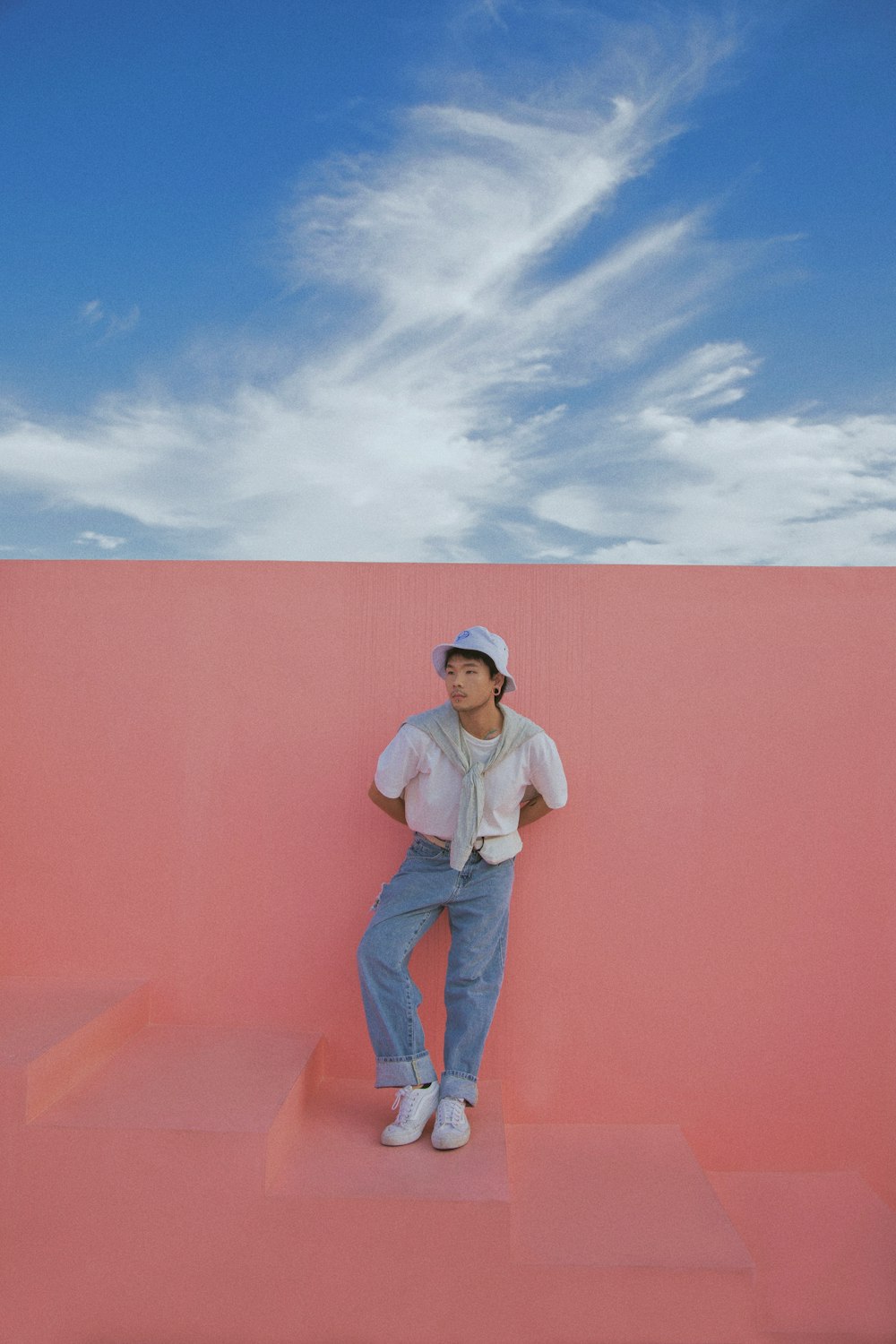 man in white dress shirt and blue denim jeans standing beside orange wall