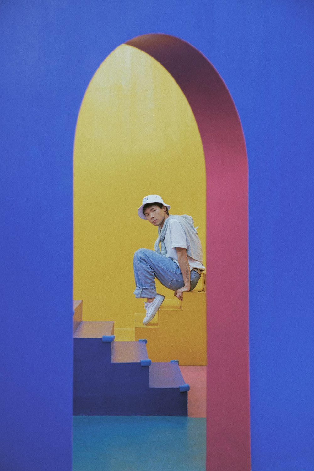 man in white t-shirt and blue denim jeans sitting on yellow and blue wall