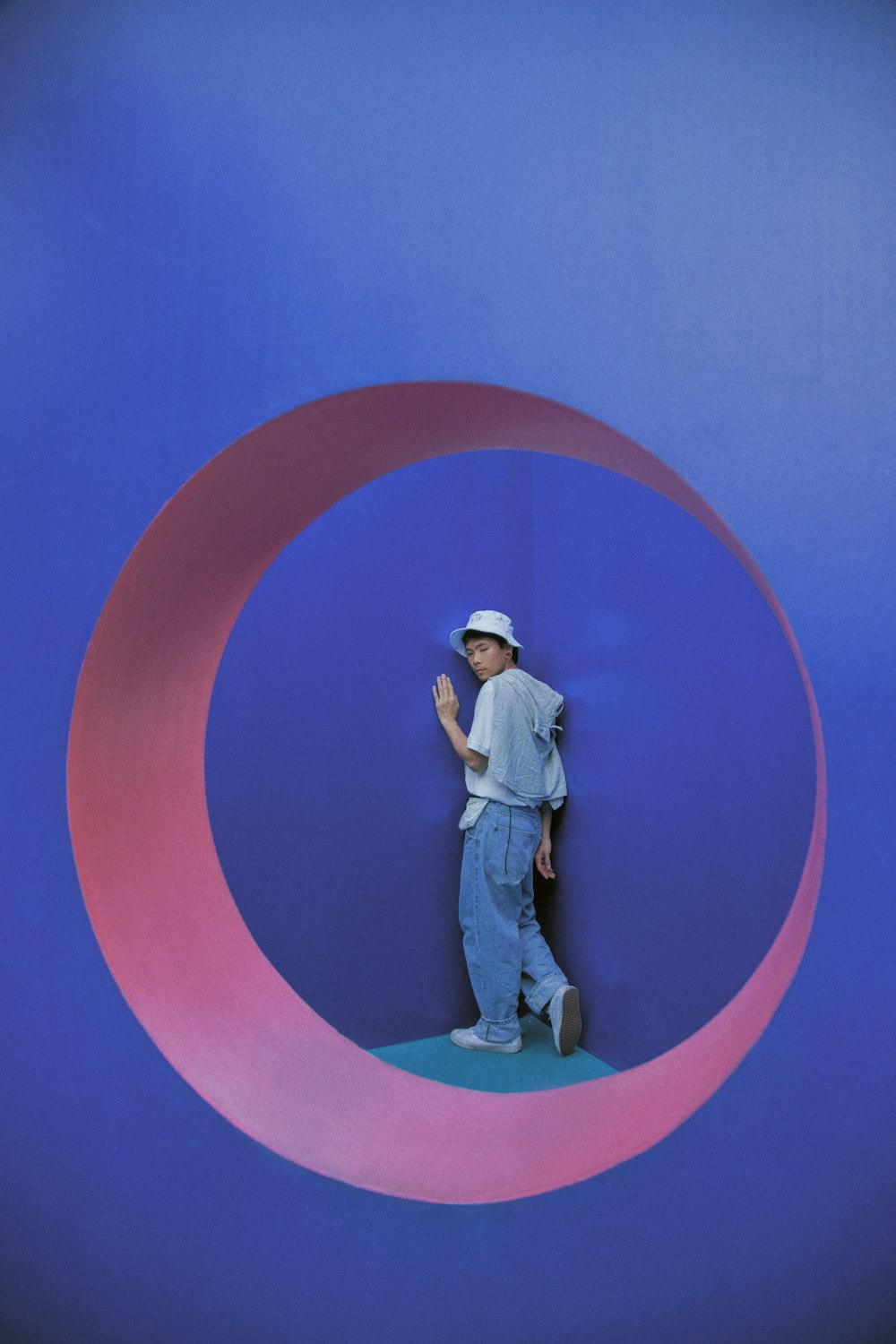 man in white t-shirt and blue denim jeans standing on blue and pink round wall
