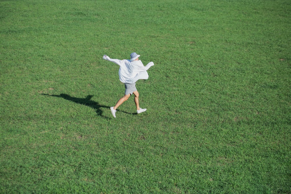 man in white shirt and shorts running on green grass field during daytime