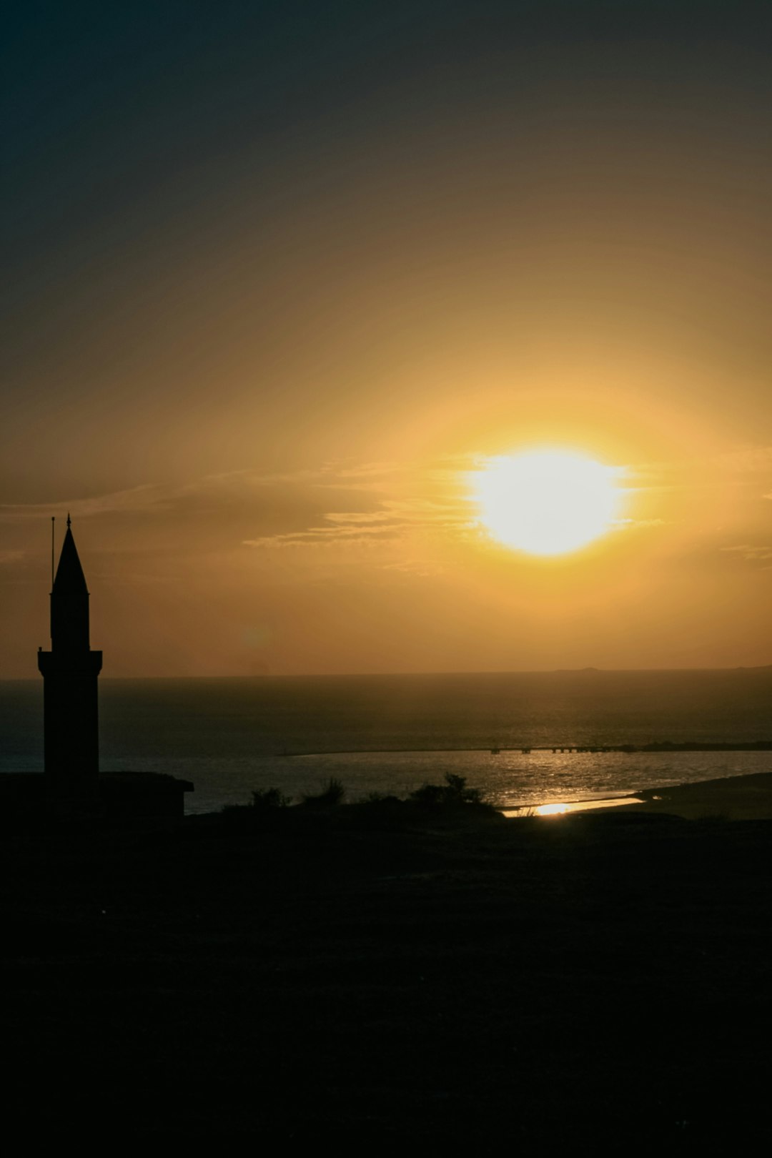 silhouette of building near body of water during sunset