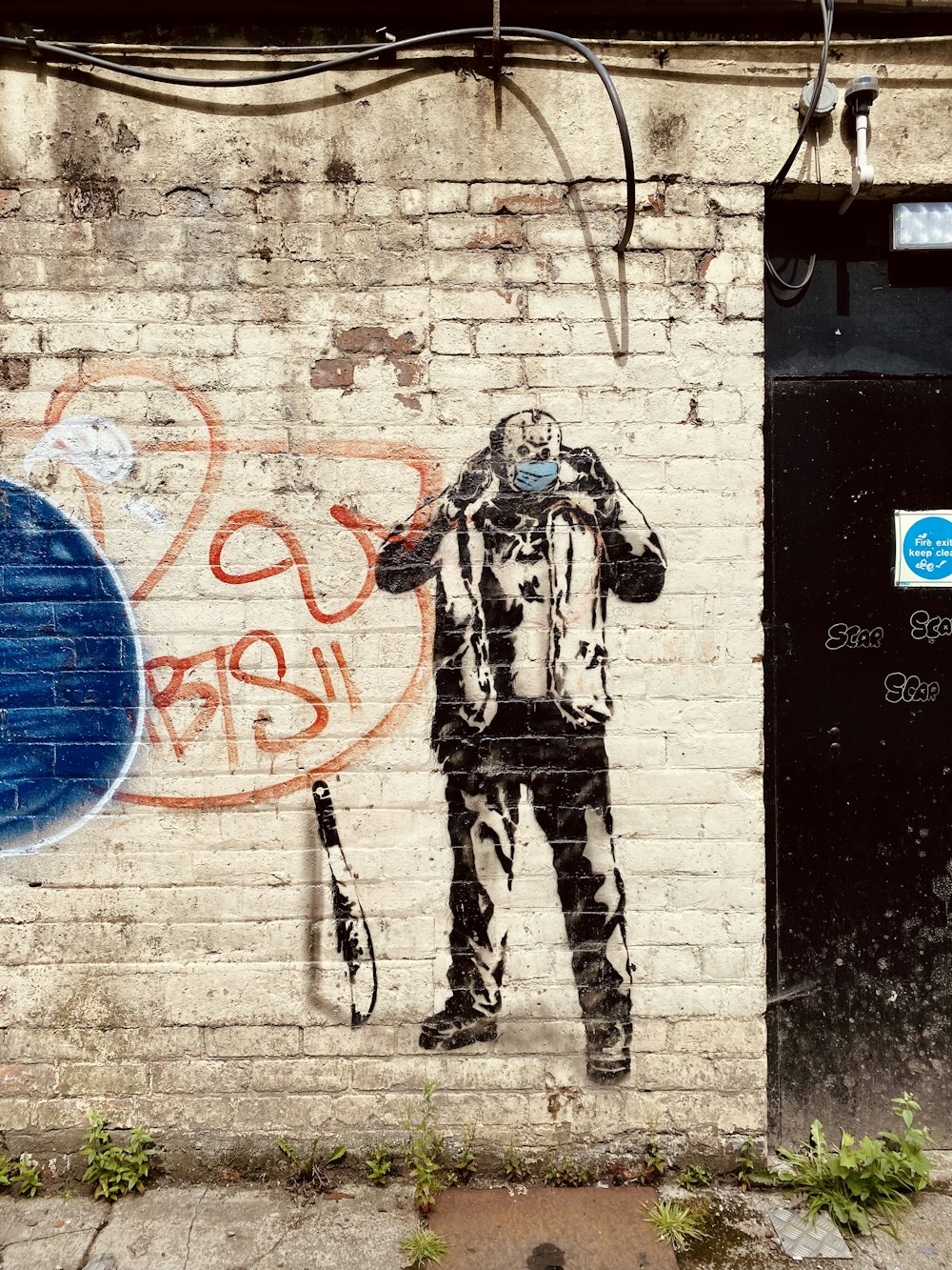 파란색과 흰색 낙서가 있는 벽 옆에 서 있는 흑백 위장 재킷을 입은 남자