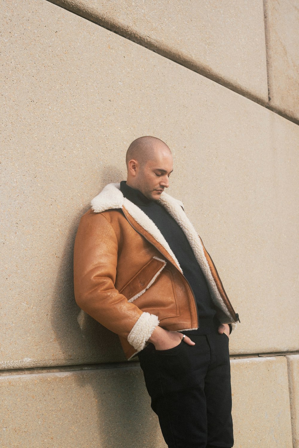 man in brown coat leaning on wall