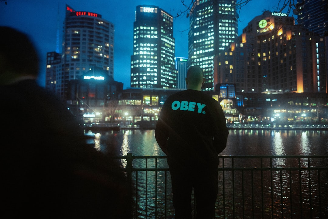 man in black and white hoodie standing in front of city buildings during night time