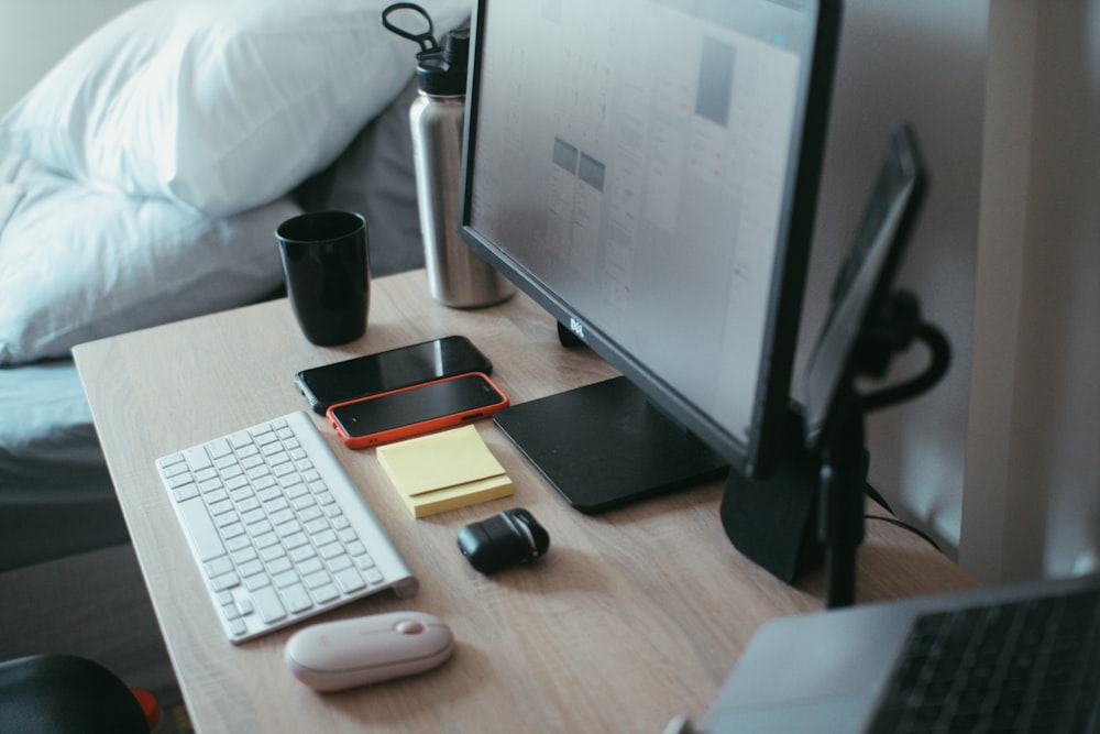 black flat screen computer monitor beside white computer keyboard on brown wooden table