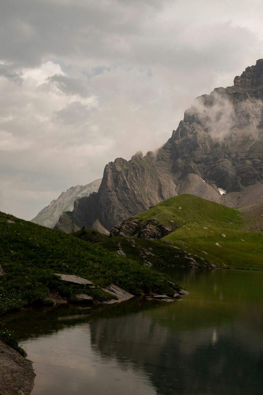 green and gray mountain beside lake under cloudy sky during daytime