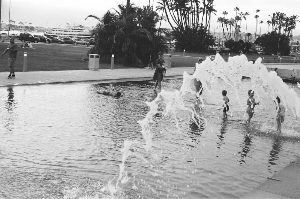 people playing on water fountain in grayscale photography