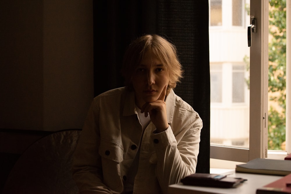 woman in white coat sitting beside window