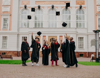 people in black academic dress standing on brown concrete floor during daytime