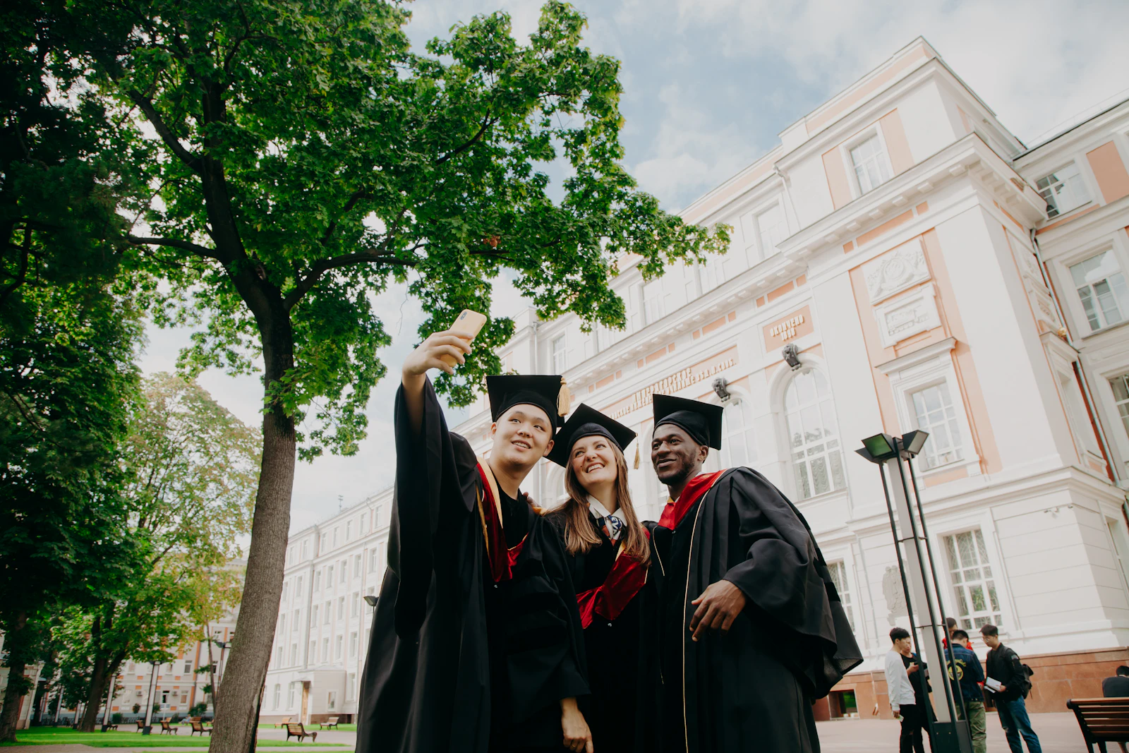 Three graduates taking a selfie in front of a university building