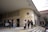 A group of people stand outside a university building with the sign 'Ankara Üniversitesi DİL ve TARİH - COĞRAFYA FAKÜLTESİ' on a stone facade. The entrance features a series of windows and a flat canopy. Some individuals are engaged in conversation while others appear to be using mobile devices. Trees without leaves and overcast sky indicate a colder season.
