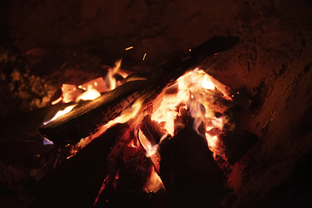 A close-up of glowing embers in a rustic fire pit, casting warm light on wooden tableware.