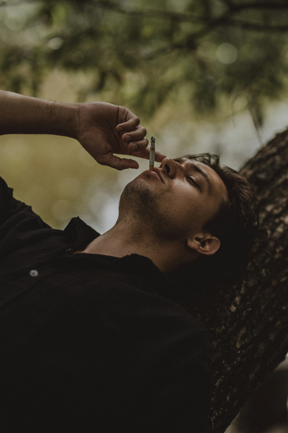 a man laying on a tree with a cigarette in his mouth