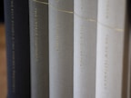 A row of neatly arranged books with varying shades of black, gray, and white covers. The titles are printed in gold lettering along the spines, suggesting a collection of religious or historical texts.