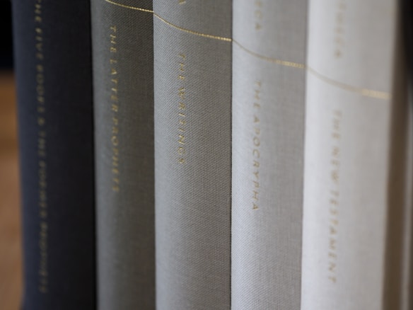 A row of neatly arranged books with varying shades of black, gray, and white covers. The titles are printed in gold lettering along the spines, suggesting a collection of religious or historical texts.
