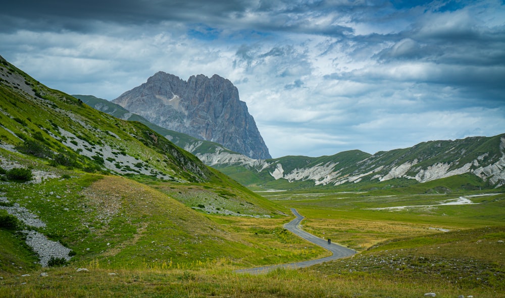 green grass field near mountain under white clouds during daytime