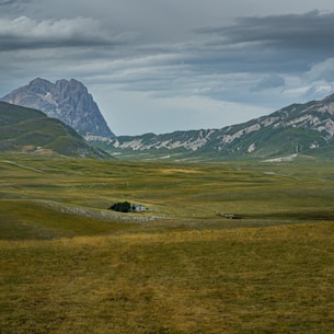 green grass field near mountain under white clouds during daytime