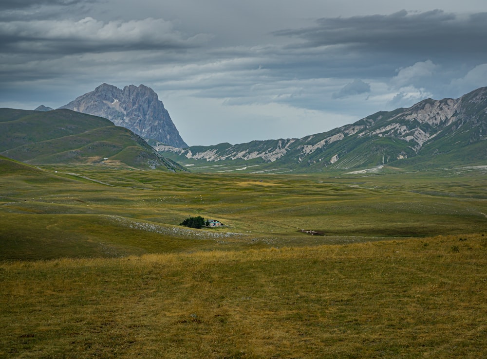 campo de grama verde perto da montanha sob nuvens brancas durante o dia