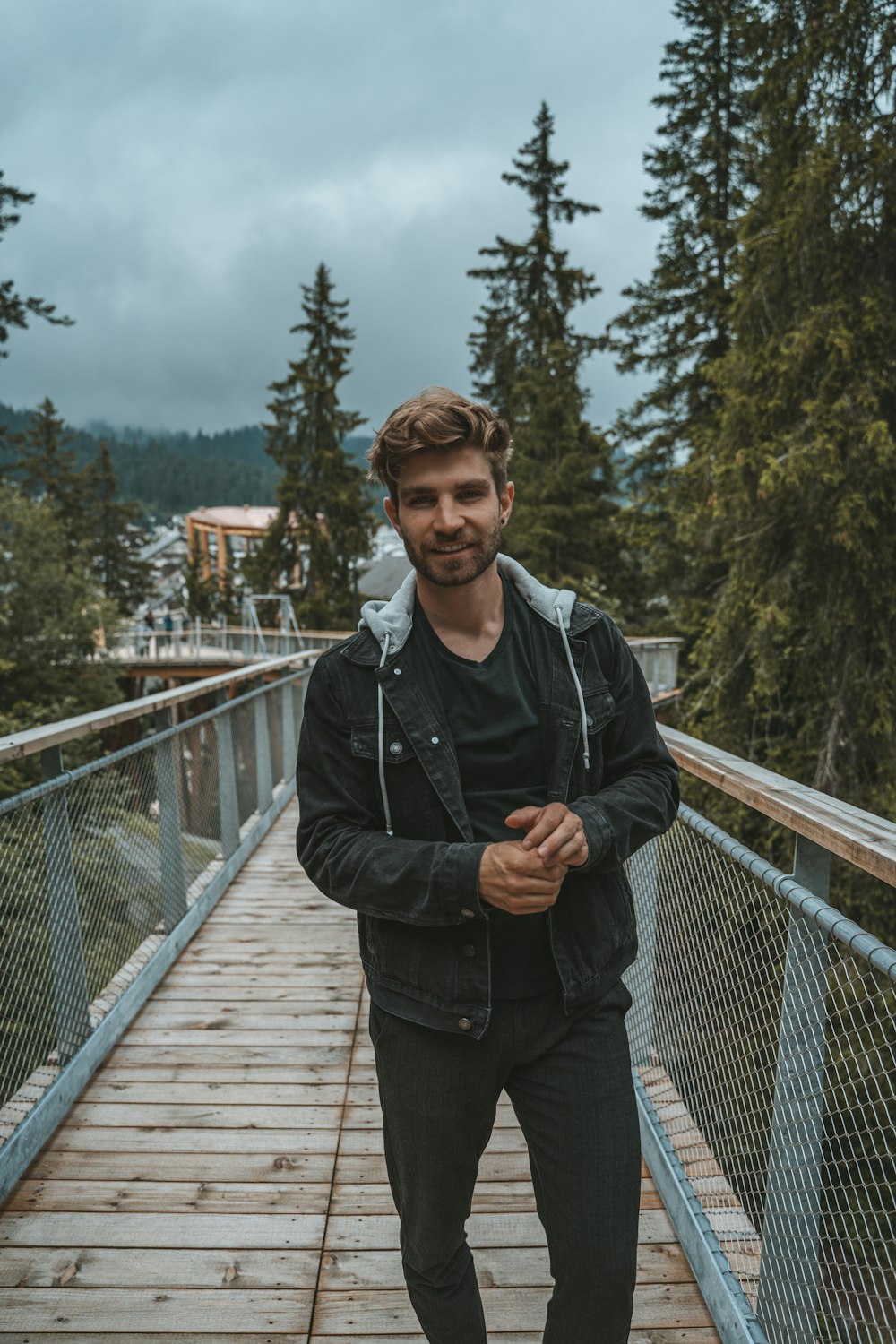 man in black jacket standing on wooden bridge during daytime