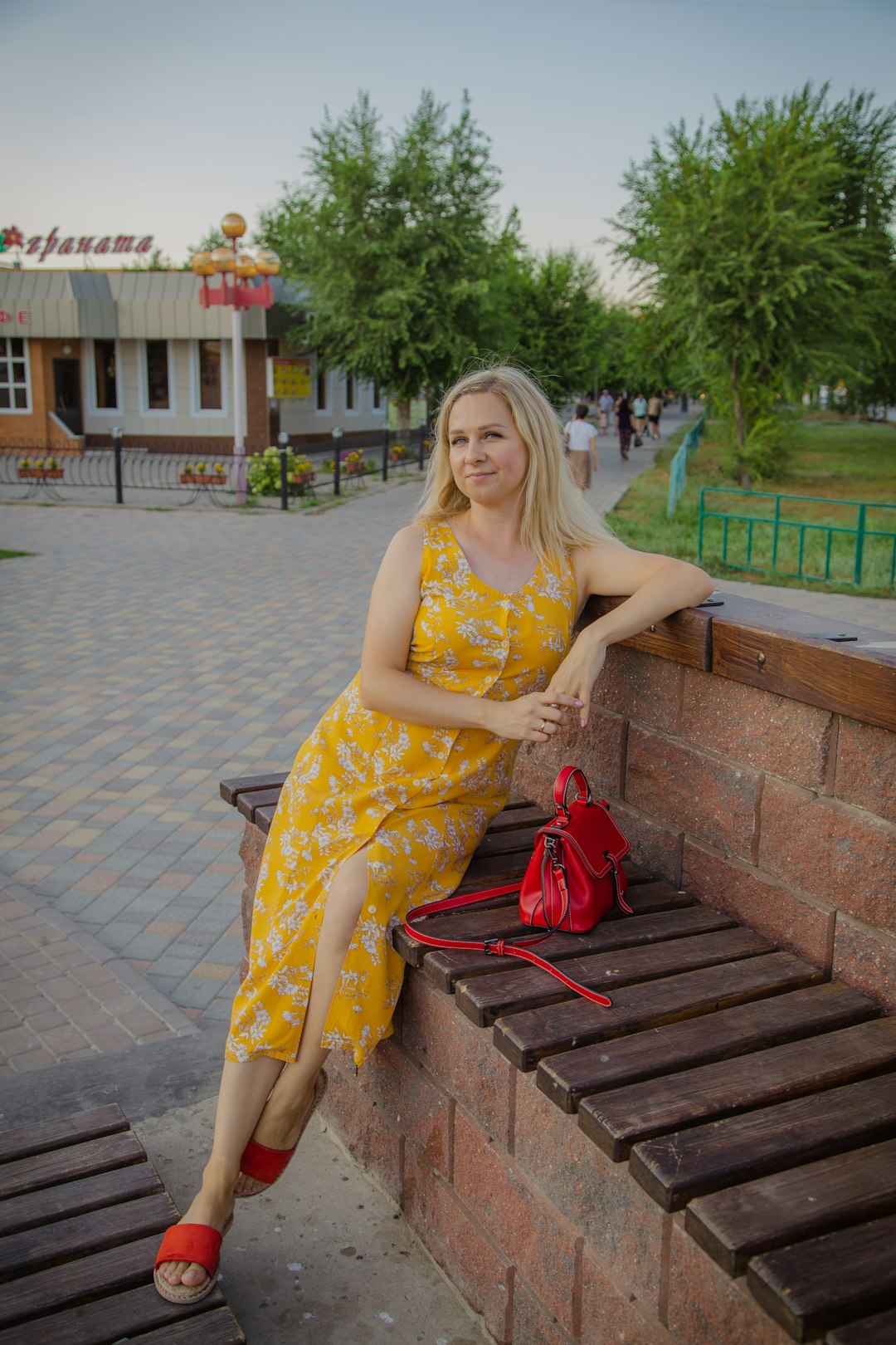 woman in yellow and white floral sleeveless dress sitting on brown wooden bench during daytime