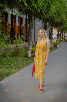 A young woman in a flowy summer dress walking through a sunlit city street, carrying a stylish tote bag.