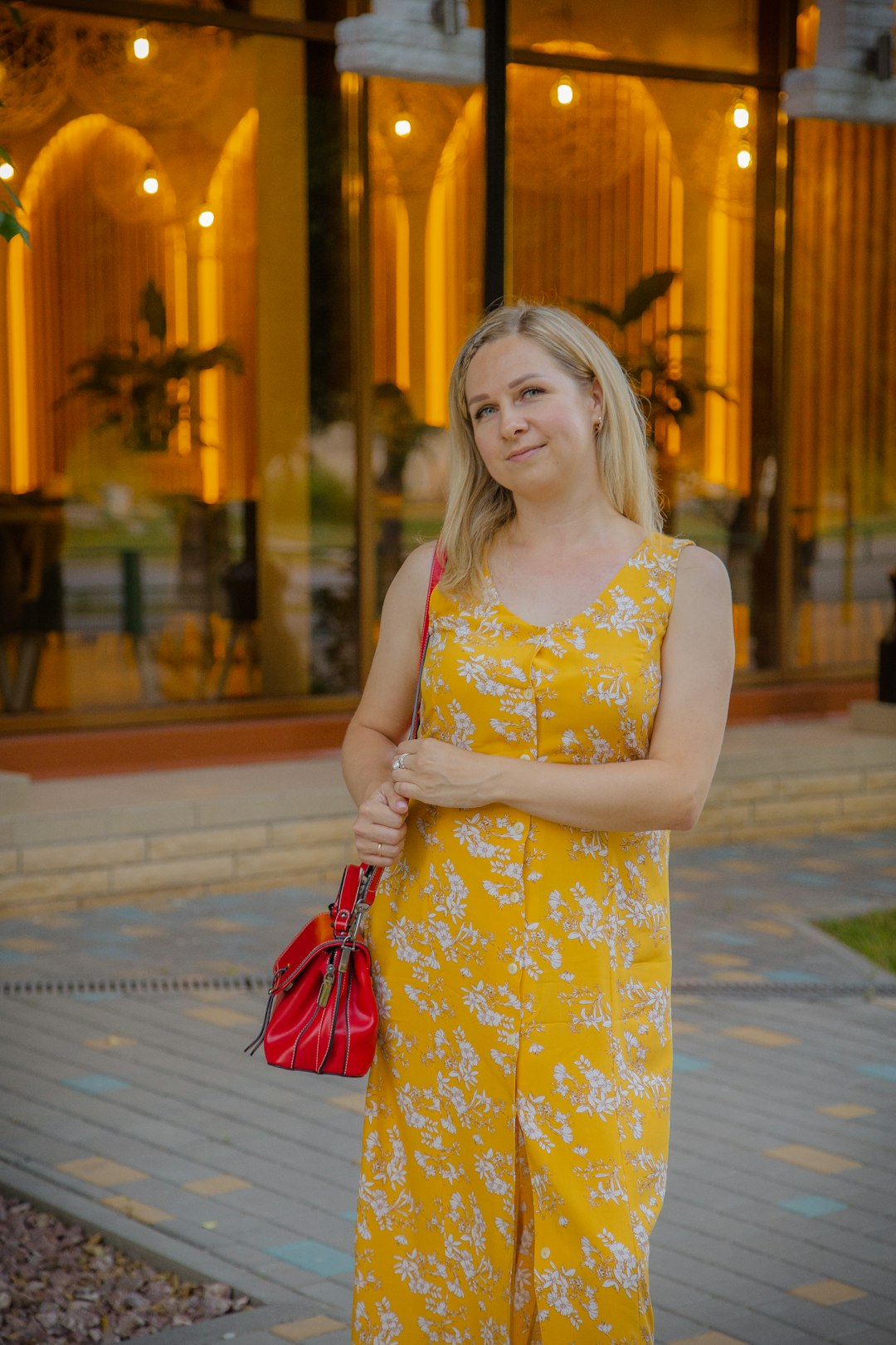 woman in yellow and white floral sleeveless dress holding red sling bag