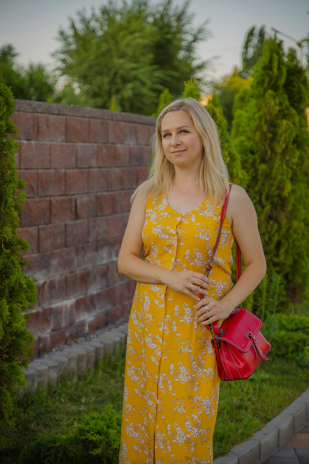 woman in yellow and white floral sleeveless dress holding red leather sling bag