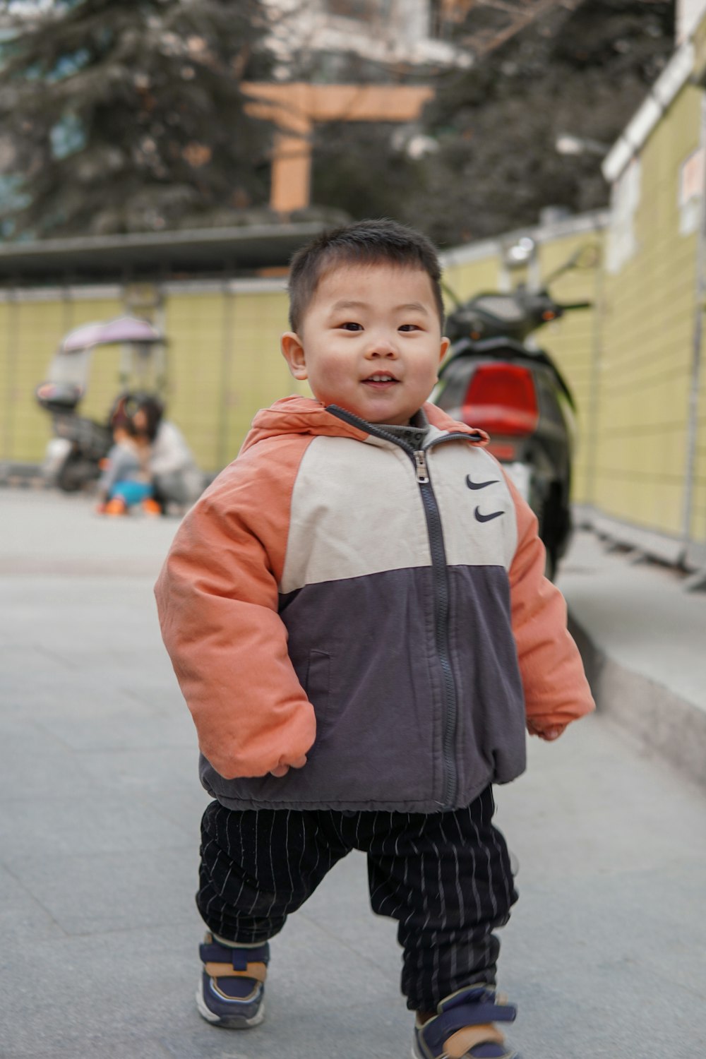 boy in orange and gray zip up jacket standing on road during daytime