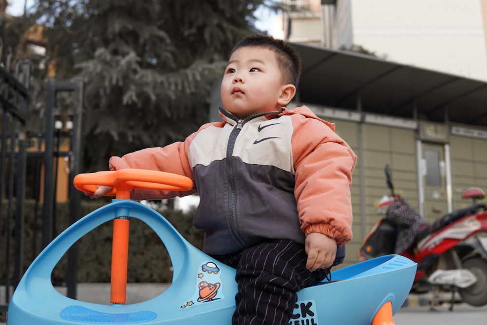 boy in red jacket riding blue ride on toy car