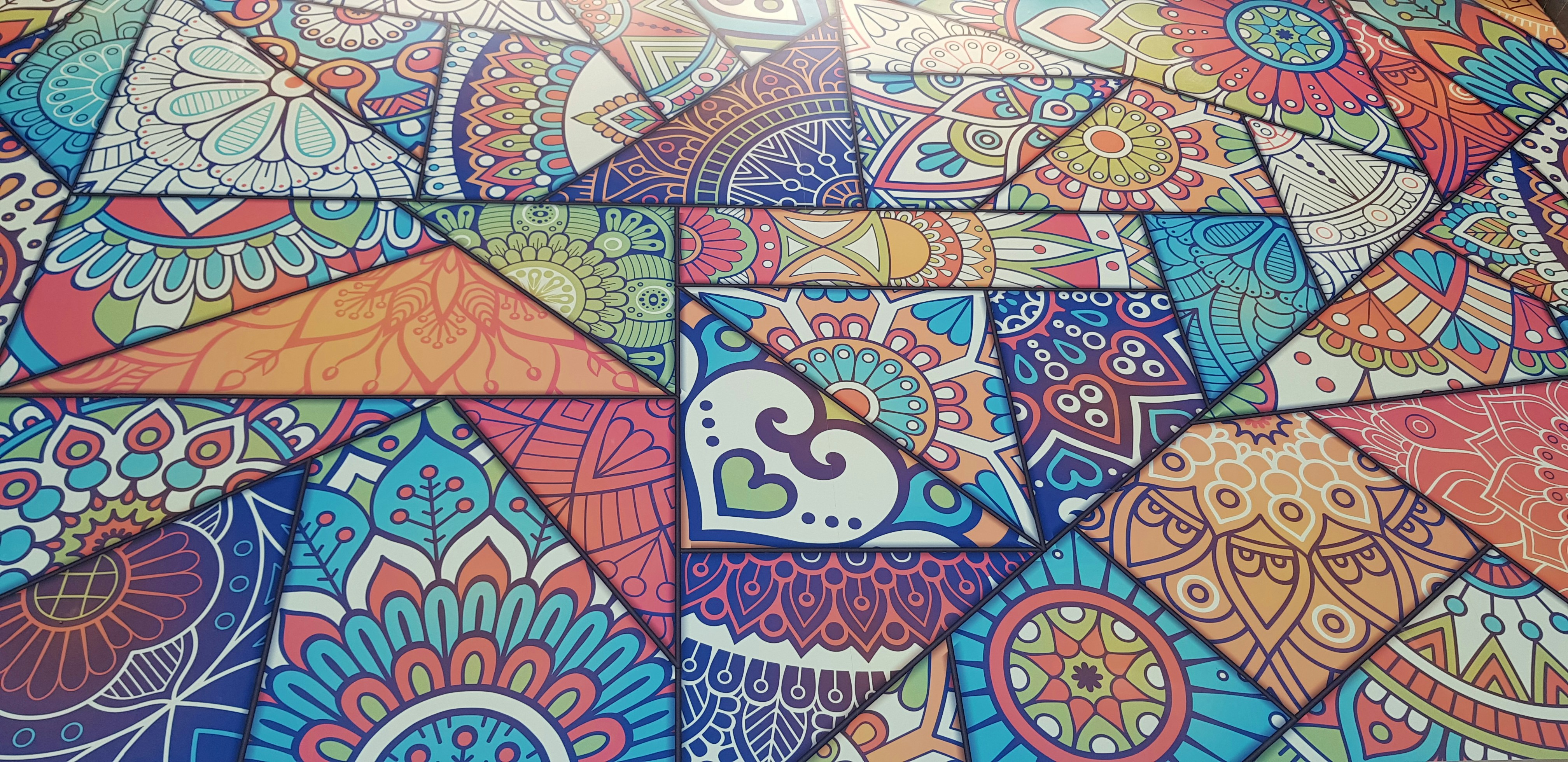 A vibrant and colorful mosaic composed of various geometric shapes and intricate patterns. Each piece features unique designs, including floral, mandala, and paisley motifs, creating a rich tapestry of artistic elements. The image is filled with both cool and warm tones, resulting in a visually engaging and dynamic composition.