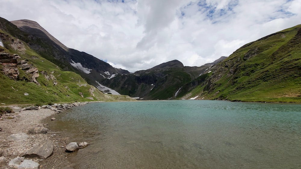 green and brown mountains beside body of water under white clouds during daytime