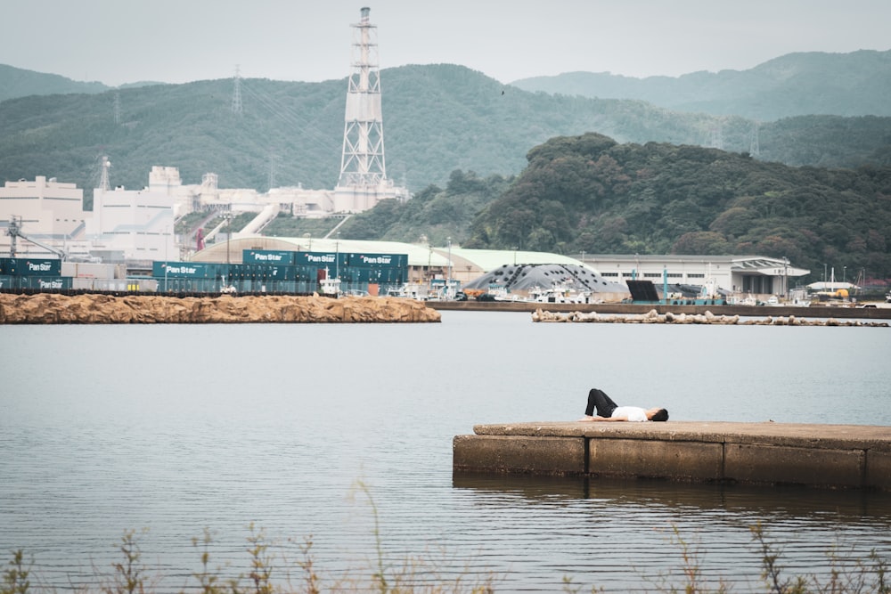 person in black pants sitting on brown concrete dock during daytime