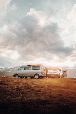 A couple standing beside their camper van overlooking a lush green valley at sunset.
